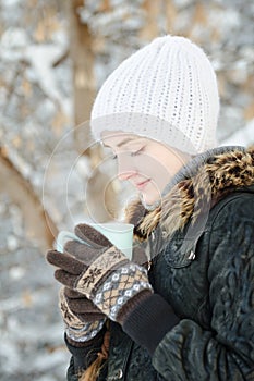 Girl in a white hat look in cup of tea. Winter, outdoors. Side v