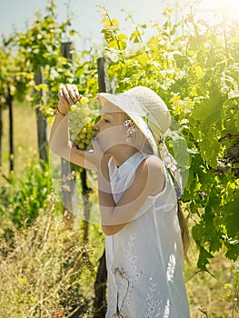 The girl in the white hat with pleasure eats green grapes on the field.