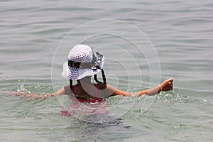 Girl in a white hat swimming in the sea. The view from the back. summer vacation