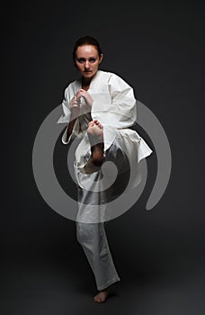 Girl in white kimono kicks forward left leg