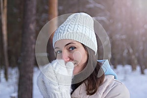 A girl in white knitted mittens and a hat. Snowy forest in the background. Winter. Snow around.