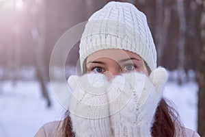 A girl in white knitted mittens and a hat. Snowy forest in the background. Winter. Snow around.