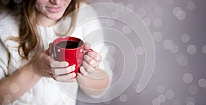 A girl in a white knitted sweater holds a red mug with tea in her hands. Copy space