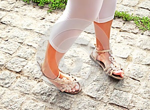 Girl in white leggings and summer sandals twists legs