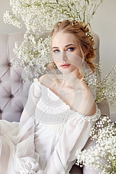 Girl white light dress and curly hair, portrait of woman with flowers at home near the window, purity and innocence. Curly blonde