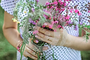 A girl in a white light dress holds a bouquet of wild flowers in her hands. depersonalized photo, midsection, copy space, photo