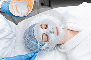 A girl in a white robe gets an alginate mask on her face