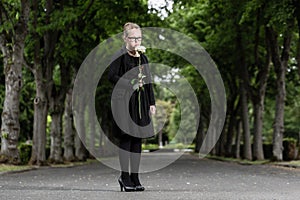 Girl with white rose mourning deceased on graveyard