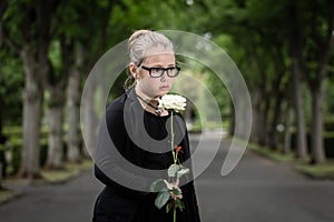 Girl with white rose mourning deceased on graveyard