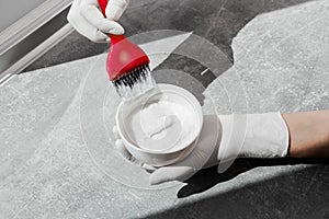 Girl in white rubber protective gloves holds a brush in her hands and mixes hair dye close-up colorist hair care at home hair dyei