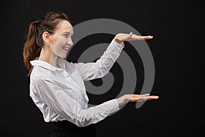 Girl in a white shirt on abstractly points to the object with her hands a black background