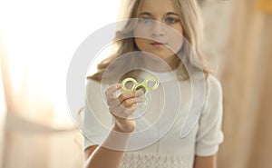 Girl in white shirt playing with green fidget spinner in bright room