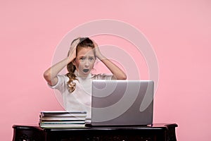 Girl in a white shirt and scaredly clings to her head on a pink background.