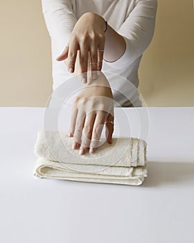 Girl in a white shirt shows her neatly and nourished hands placed on the cream towel.