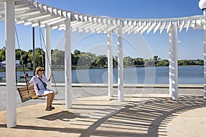 girl in a white shirt and a straw hat is swinging on a swing in the park under a white canopy that protects from the sun