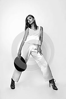 Girl in a white suit and black hat in the studio on a white background. Black and white photo