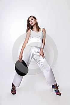 Girl in a white suit and black hat in the studio on a white background.