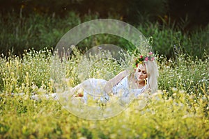 Girl in a white sundress and a wreath of flowers on her head sit