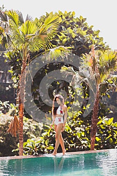 Girl in white swimsuit walking edge infinity pool