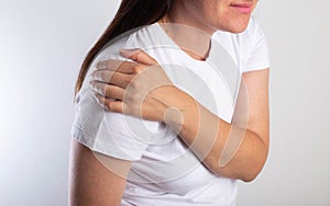 A girl in a white T-shirt is holding her shoulder joint and is in severe pain. Concept of habitual shoulder dislocation