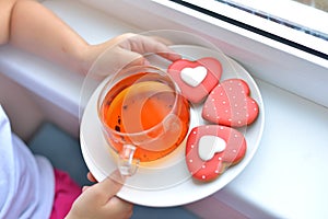 A girl in a white T-shirt holds a cup of tea and a liver in the form of a red heart.