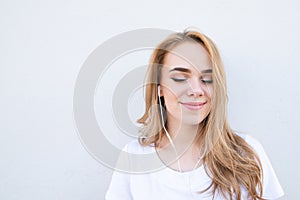 Girl in a white T-shirt, listens to music in her headphones with her eyes closed and smiles on a white background