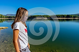 Girl with a white t-shirt and a mask to protecet herself from the coronavirus posing in a lake with the forest reflected in the