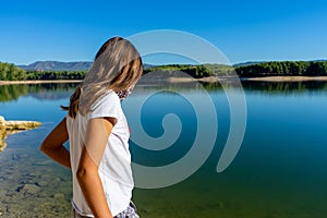 Girl with a white t-shirt and a mask to protecet herself from the coronavirus posing in a lake with the forest reflected in the
