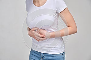 A girl in a white T-shirt massages her stomach with her hands. Belly pain. The concept of poisoning. Muscle spasm