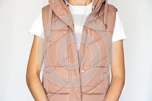 A girl in a white T-shirt and a pink warm vest stands on a white background, fashionable warm women's clothing, autumn vest,