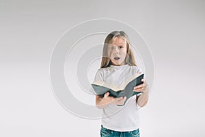 Girl in white t-shirt is reading a book on a white background. Child likes to read books