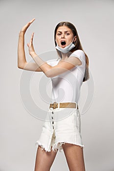 Girl in a white T-shirt and shorts with a medical mask wide open mouth gesticulate with hands