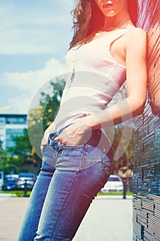 Girl in white tank shirt and blue jeans outdoor summer day  lean on tiled wall