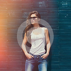 Girl in white tank shirt sunglasses and blue jeans outdoor summer day  lean on tiled wall