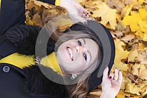 Girl white toothed smile, young happy woman whitened teeth in black hat lying in orange leaves in autumn park.