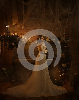 A girl in a white vintage dress with open shoulders stands against the background of an old piano and candles. Gothic