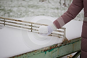 Girl in winter clothes for a walk. He holds a snowball in his hands. Standing near a concrete tennis table. Everything is covered