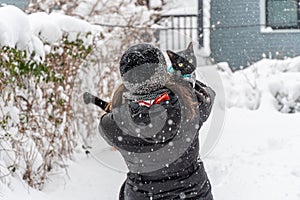 Girl in winter clothing holding black cat in snow storm