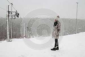 Woman in winter coat standing on slope near loop-line ski lift during snowfall. beautiful winter view in snowy weather. Mountain photo