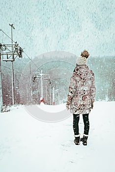 Girl in winter coat standing on slope near loop-line ski drag during snowfall. beautiful winter view in snowy weather. Mountain photo