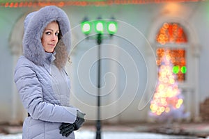 Girl in a winter jacket costs against a garland