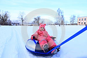 A girl in a winter overalls sits on a tubing.