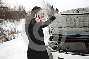 Girl on the winter road is calling the phone near the car