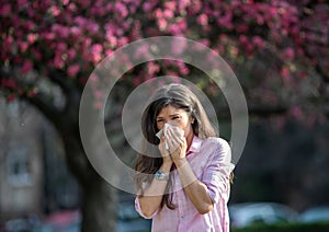 Girl wiping nose in front of blooming tree in spring