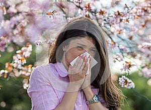 Girl wiping nose in front of blooming tree in spring