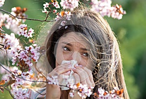 Girl wiping nose in front of blooming tree in spring