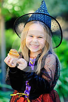 Girl in witch costume eat cupcake on Halloween