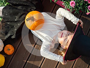 Girl in witch costume lying with pumpkin on wooden terrace