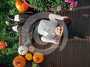 Girl in witch costume lying with pumpkin on wooden terrace