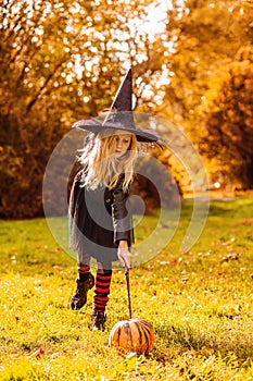 A girl in a witch costume says a spell and enchants a pumpkin with a magic wand photo